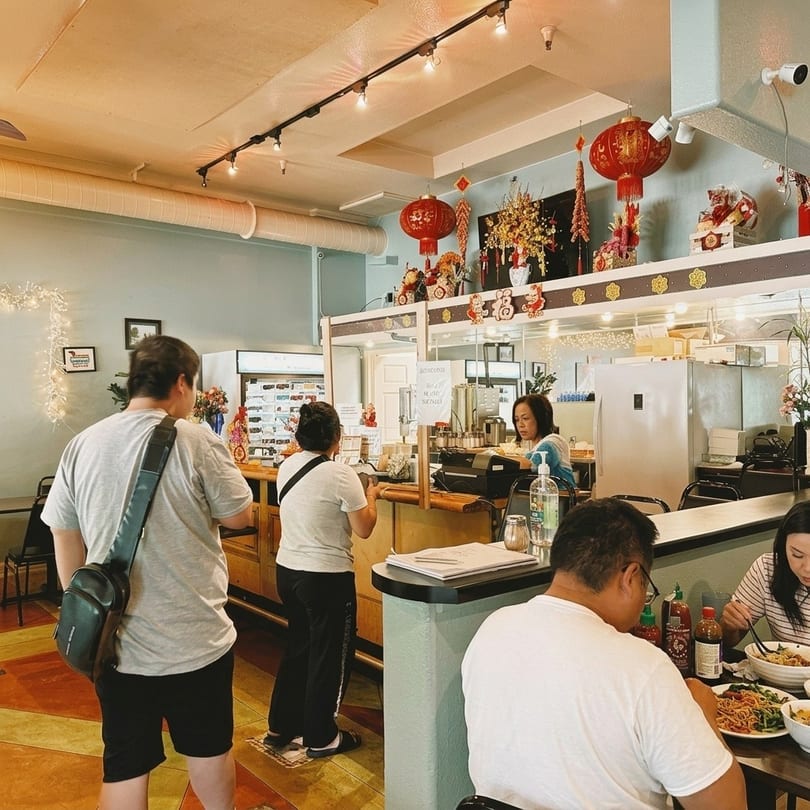 Customers ordering and dining inside a brightly lit restaurant decorated with red lanterns and flowers.