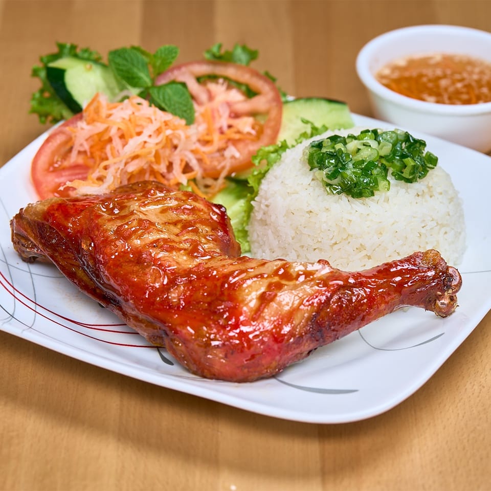 A Vietnamese dish with a glazed chicken leg, white rice, and a side salad on a white plate.