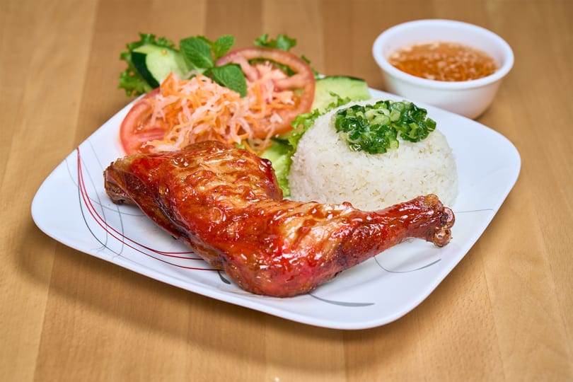A Vietnamese dish with a glazed chicken leg, white rice, and a side salad on a white plate.