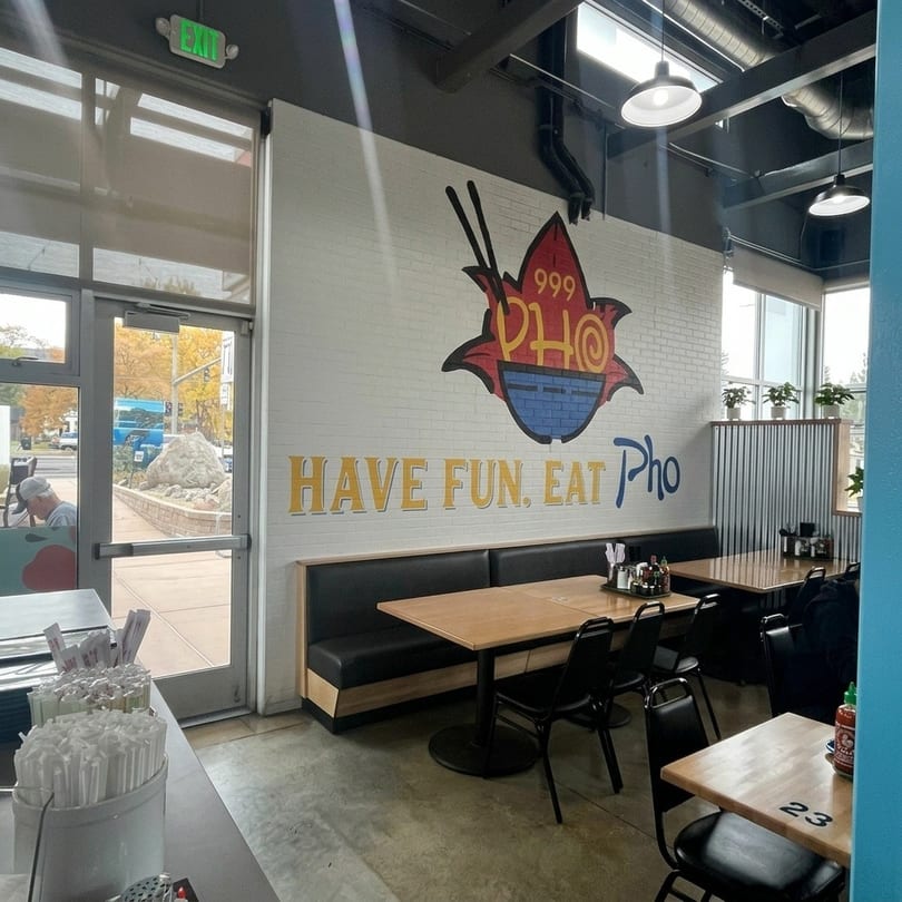 Interior of a Pho restaurant with a large mural, booths, tables, and an exit door.