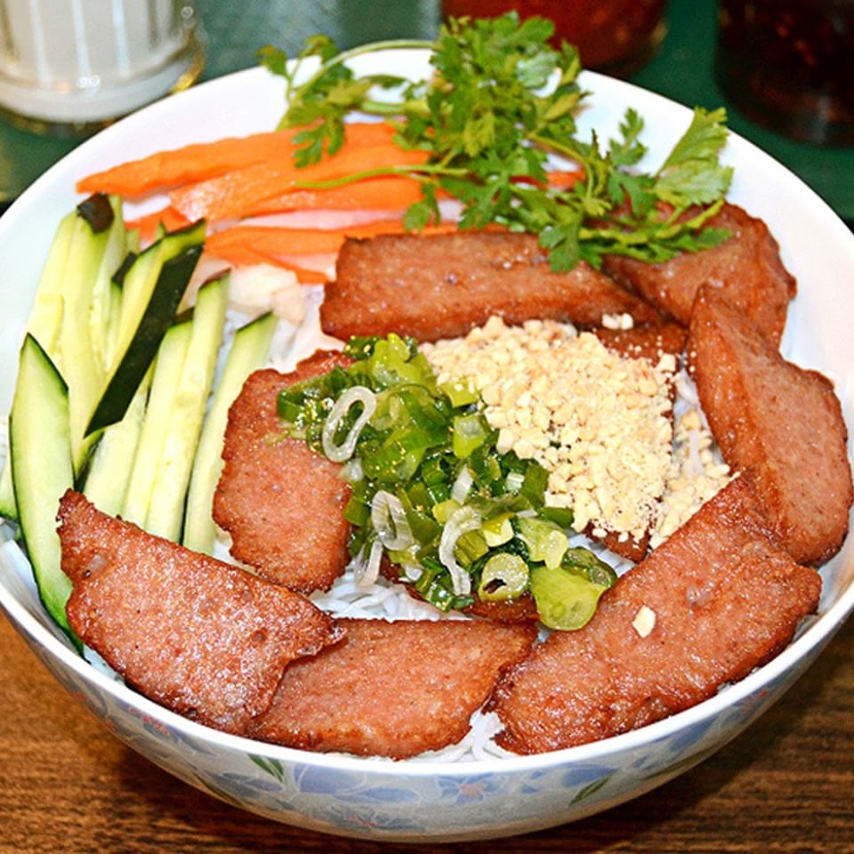 Vietnamese noodle bowl with grilled pork, fresh herbs, cucumber, carrots, and crushed peanuts.