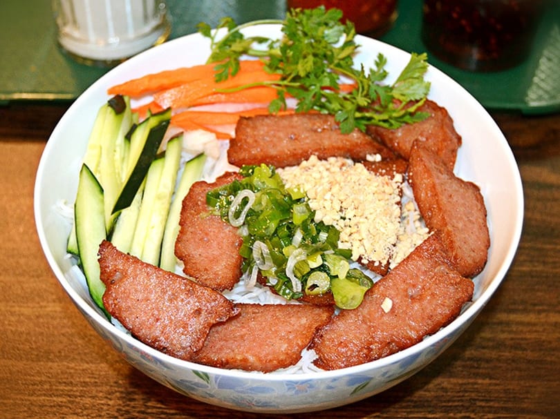 Vietnamese noodle bowl with grilled pork, fresh herbs, cucumber, carrots, and crushed peanuts.