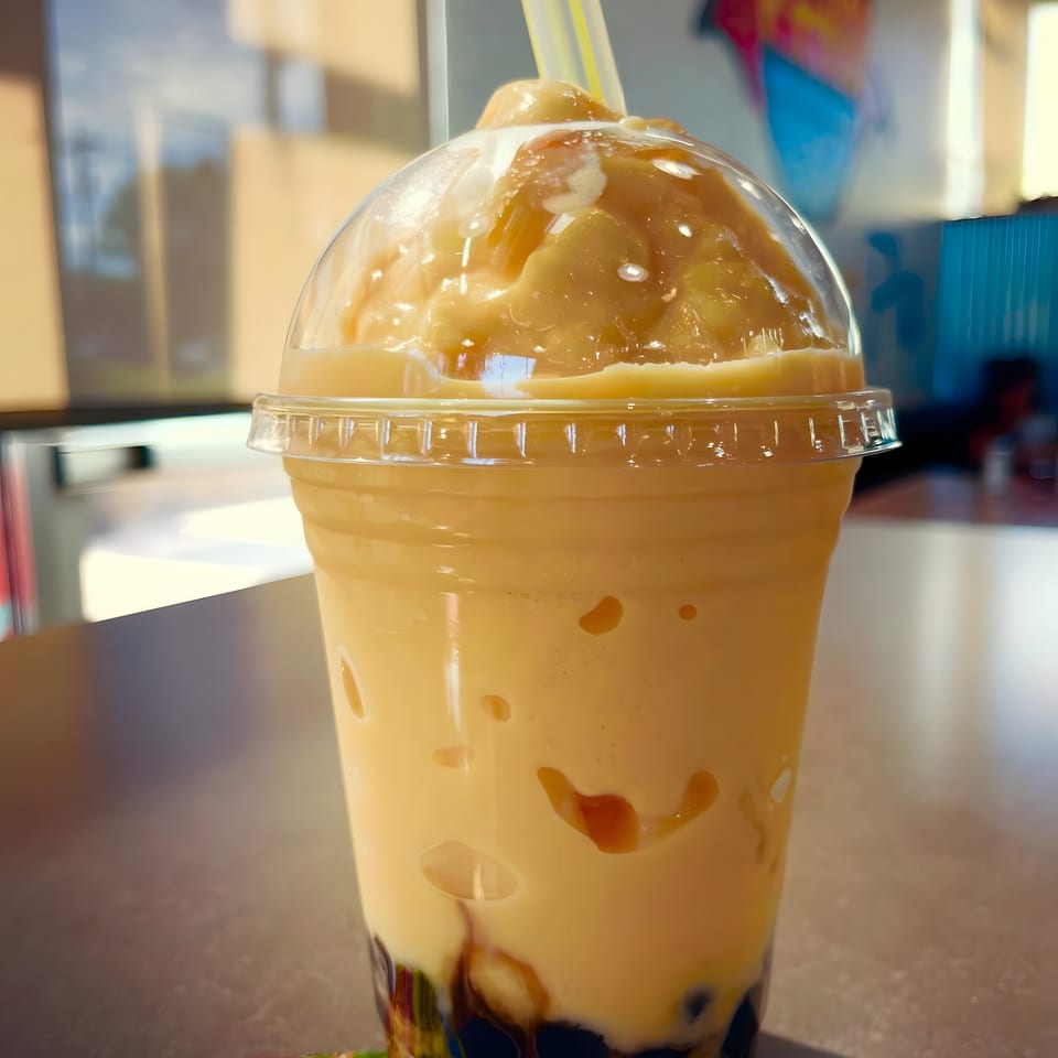 A large mango boba tea with a yellow straw sits on a table at 999 Pho.