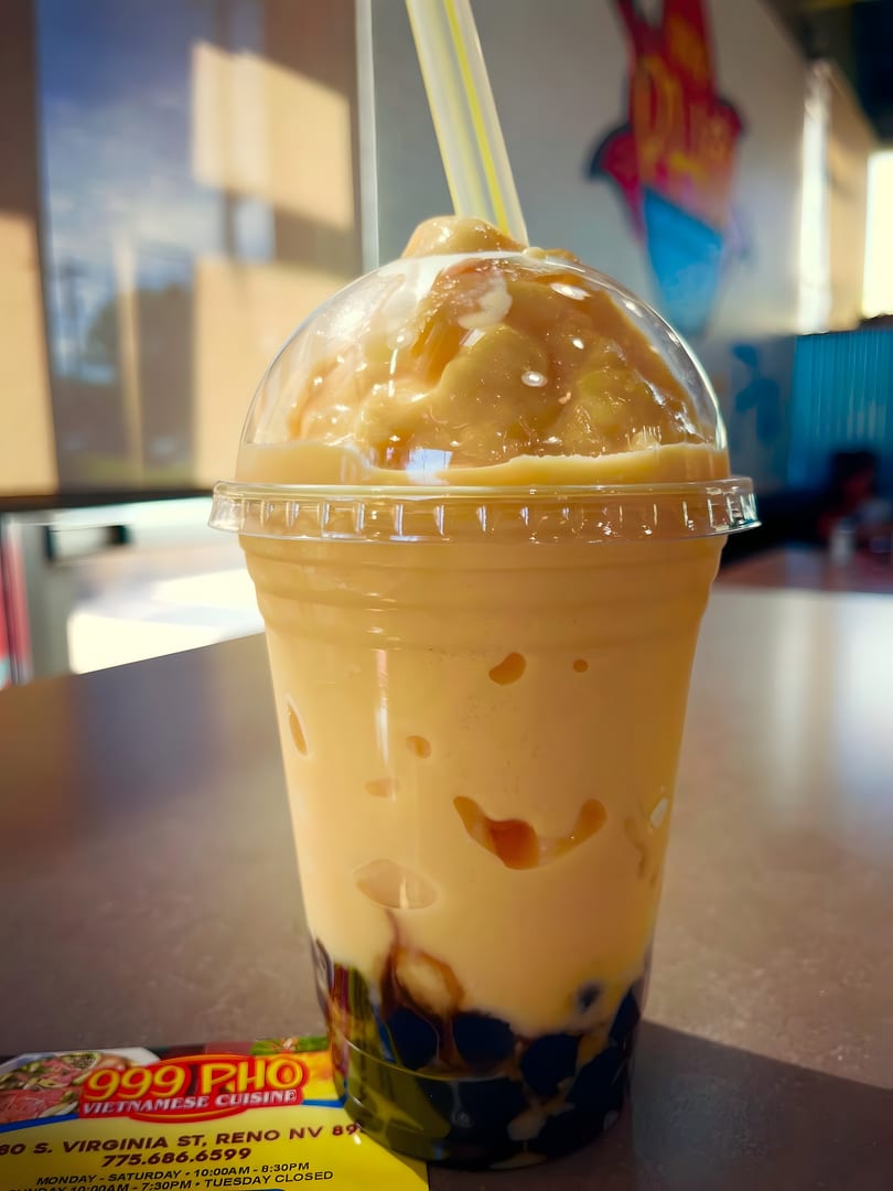 A large mango boba tea with a yellow straw sits on a table at 999 Pho.