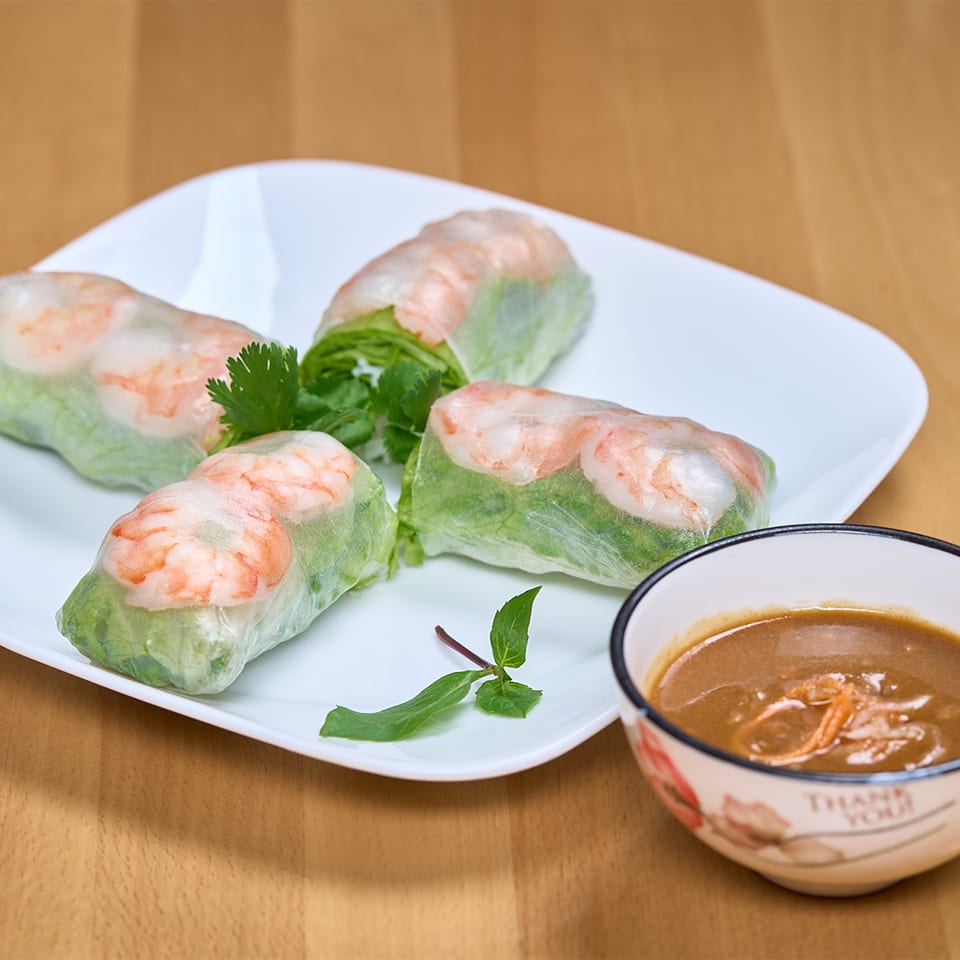 Four fresh spring rolls with shrimp and lettuce on a white plate, with a side of peanut sauce.