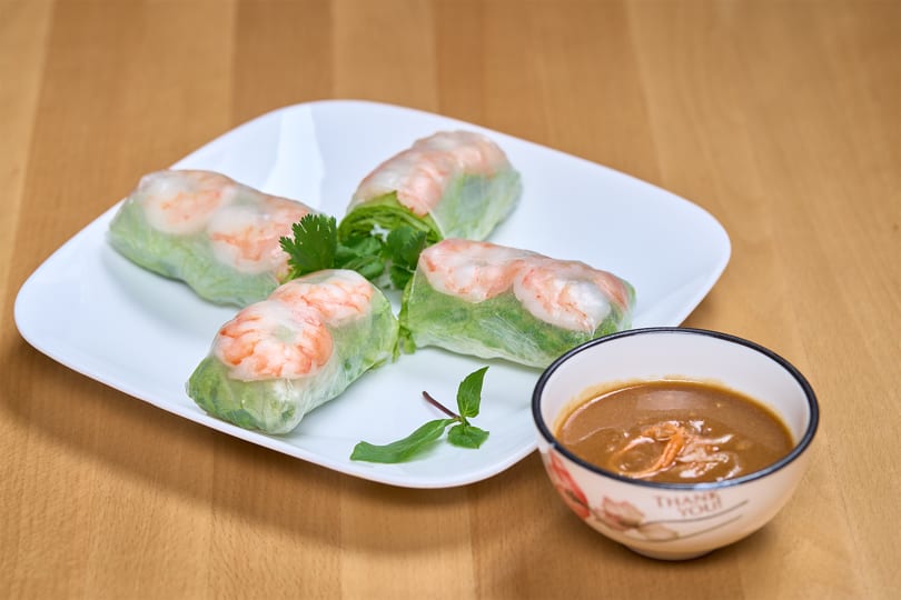 Four fresh spring rolls with shrimp and lettuce on a white plate, with a side of peanut sauce.
